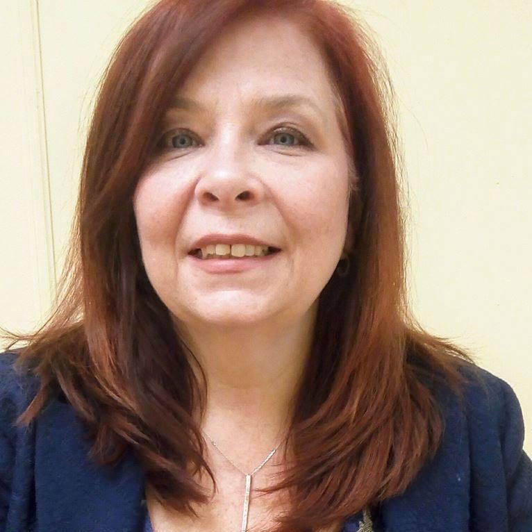 Barbara Mclean, contributor, red hair past her shoulders, in a blue blazer, against a neutral background