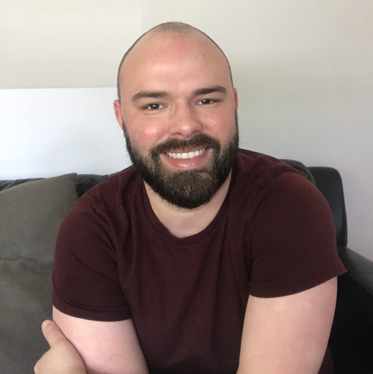 Brendan McHugh, story contributor, wearing a maroon T-shirt, sitting on a sofa in front of a neutral background.