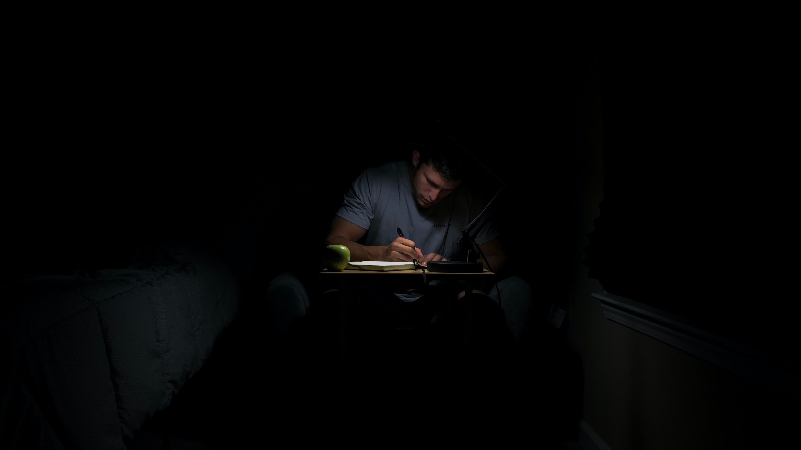 Man in a dark room writing in a journal. 