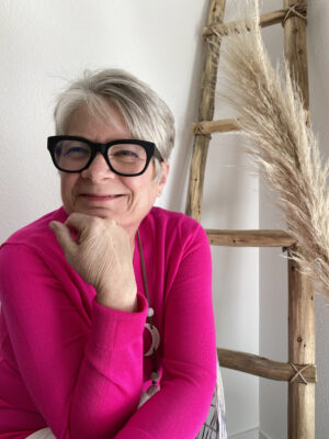 Dee-Dee Stout, story contributor, wearing thick black eyeglasses and a bright magenta top.