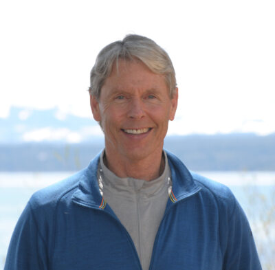 Gary Gilbert, story contributor, outdoors with a body of water blurred in the background, wearing blue 3/4 zip over a gray shirt