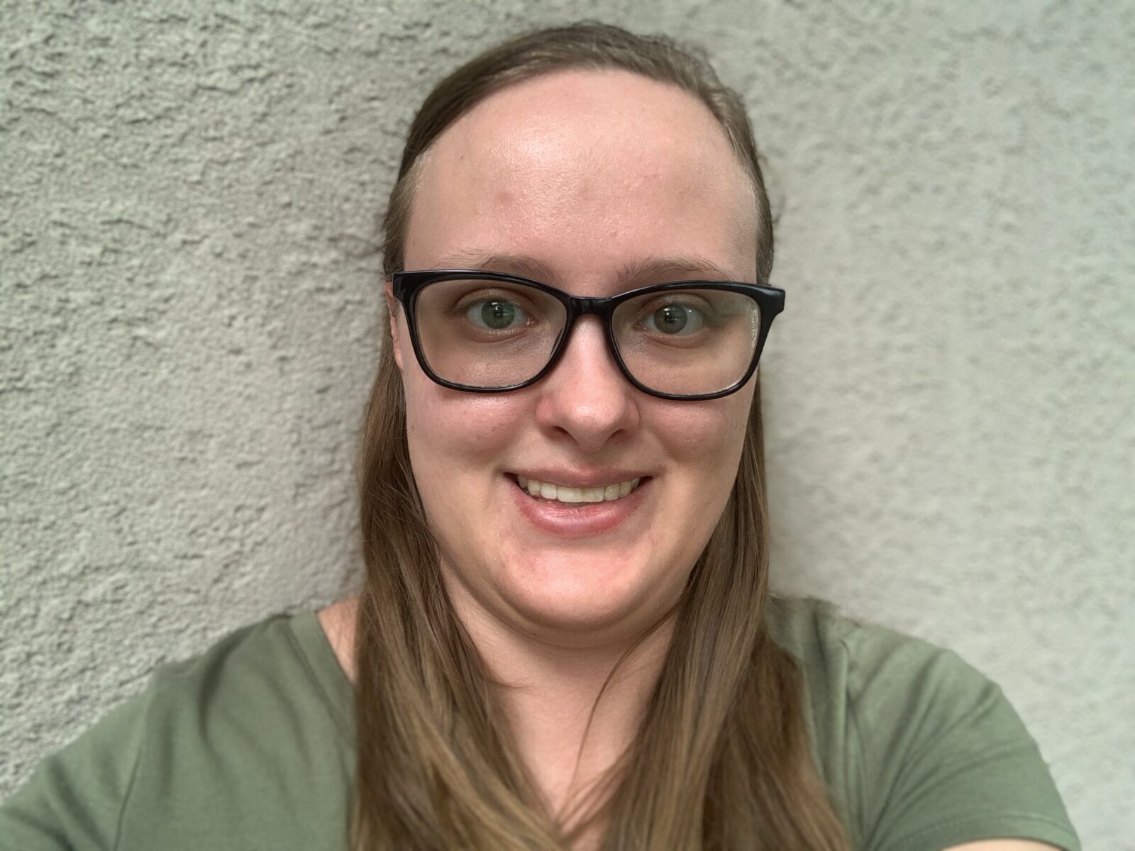 Hollyn Donovan, contributor, with long blond hair, dark-framed glasses, and a sage green t-shirt, against a neutral background.