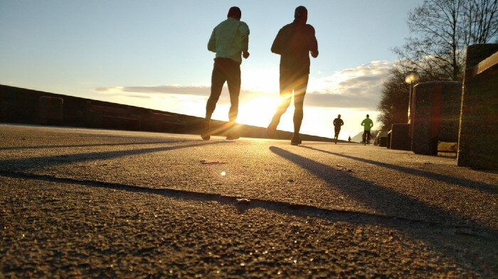 Runners on a jogging path with the sun's reflection between them. 