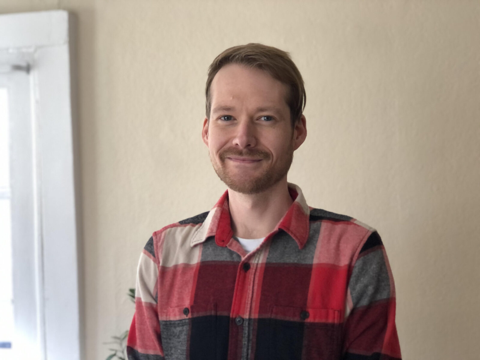 Portrait of Jason Wood, story contributor, wearing red plaid shirt standing in front of a neutral background.