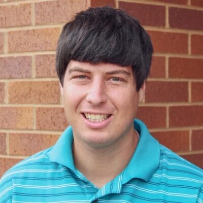 Headshot of Ryan Zadrazil, story contributor, wearing a teal striped polo shirt and standing in front of a brick wall.