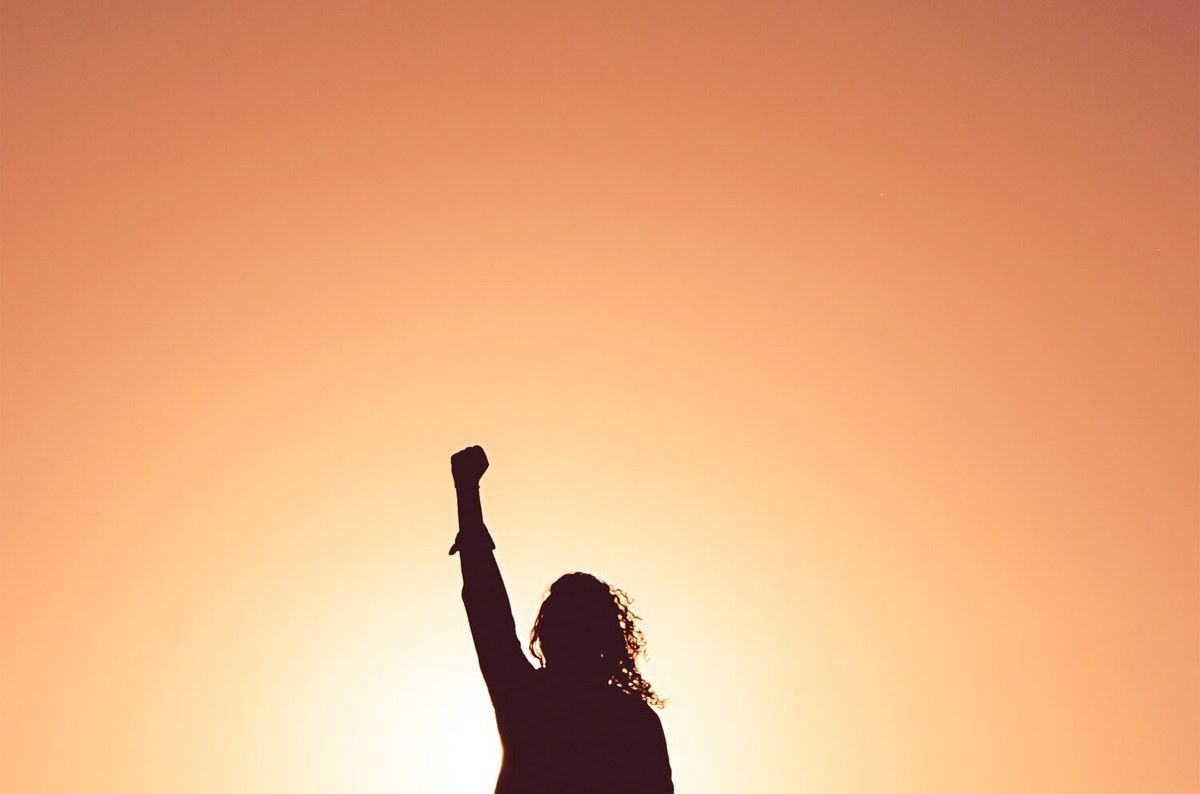 Silhouette of a woman with her fist in the air in front of a bright background.