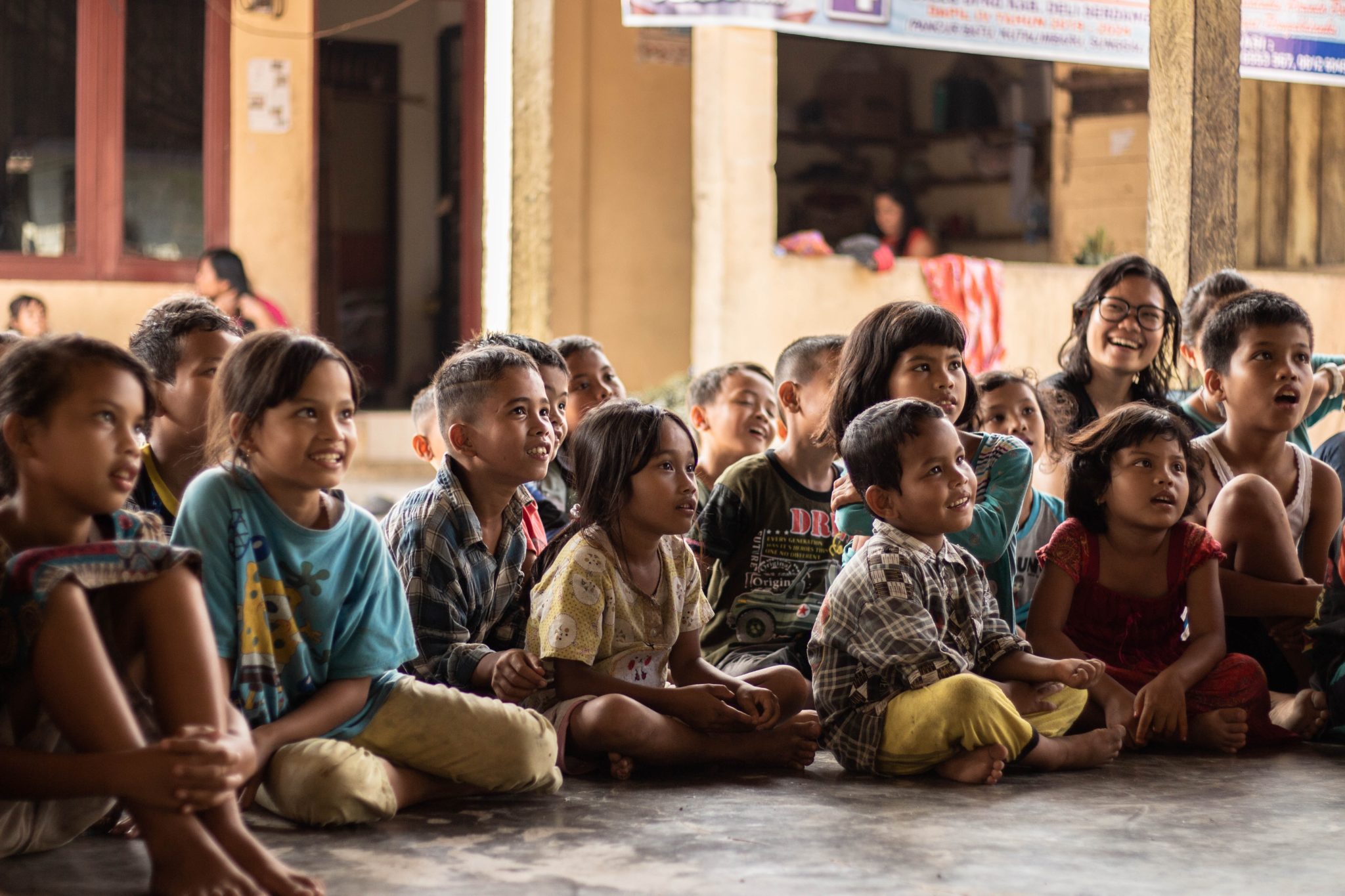 Young children gathered around outside, listening to the teacher.