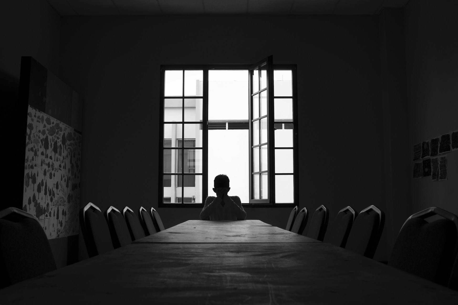 Silhouette of a person sitting in an empty room on a chair in front of a table.