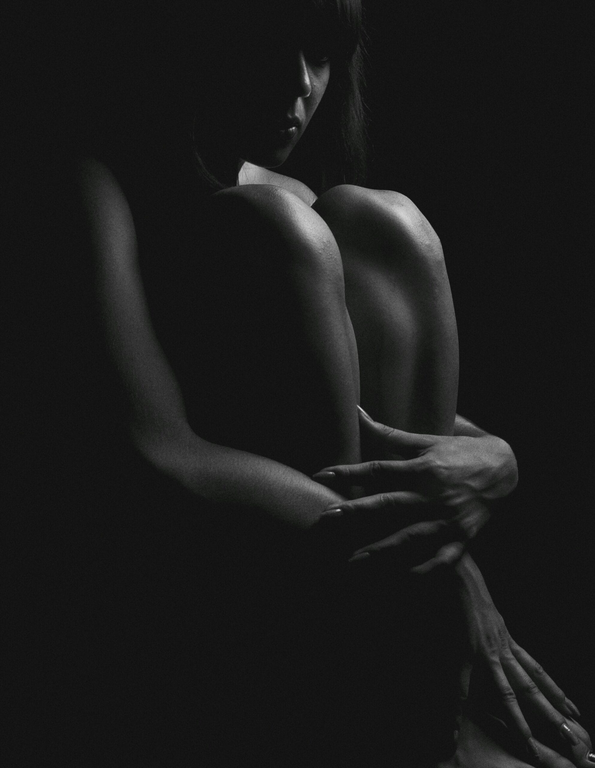 Woman sitting on floor hugging her knees to her chest. 