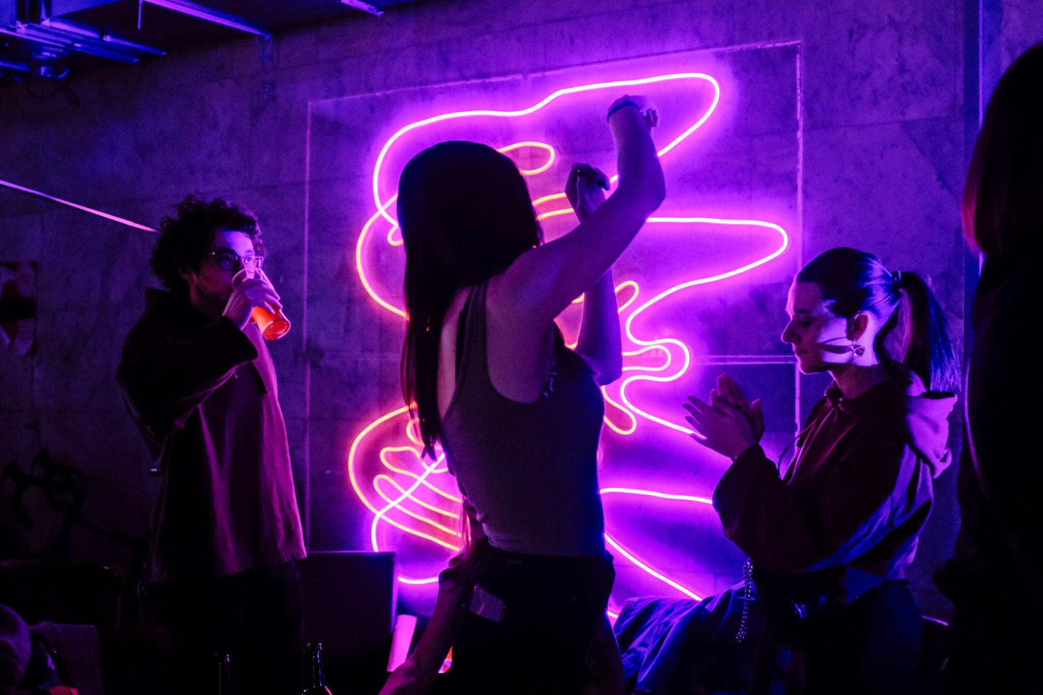 Person dancing and hanging out with friends at a party illuminated by neon lights.