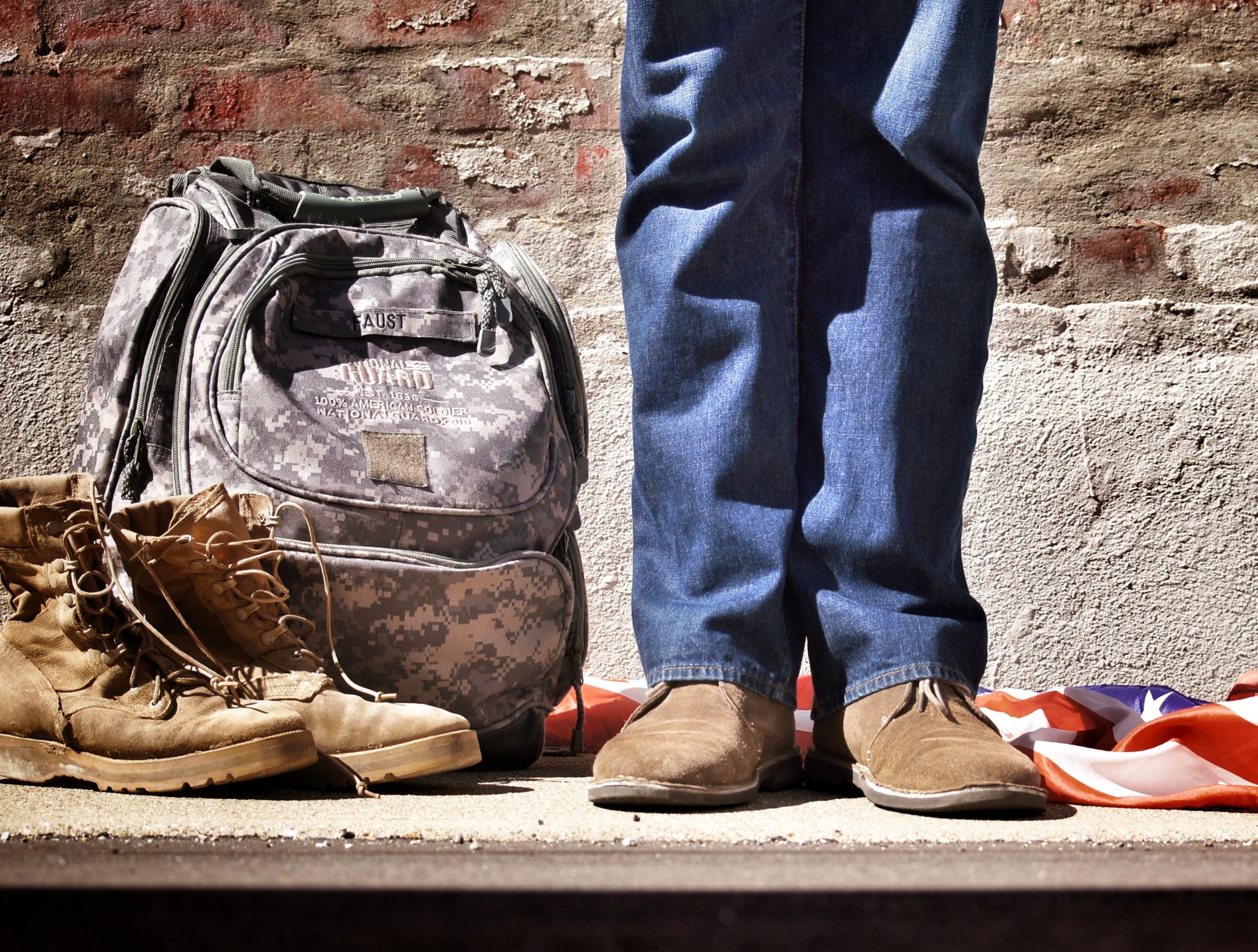 Woman standing next to military boots, a camouflage backpack, and the American flag.