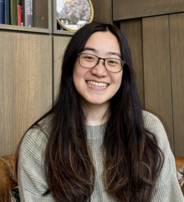 Christine Lee, sitting, with long brown hair, smiling.