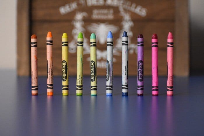 A colorful row of 10 crayons standing on upright on a blue semi-reflective table with a blurry wooden backdrop