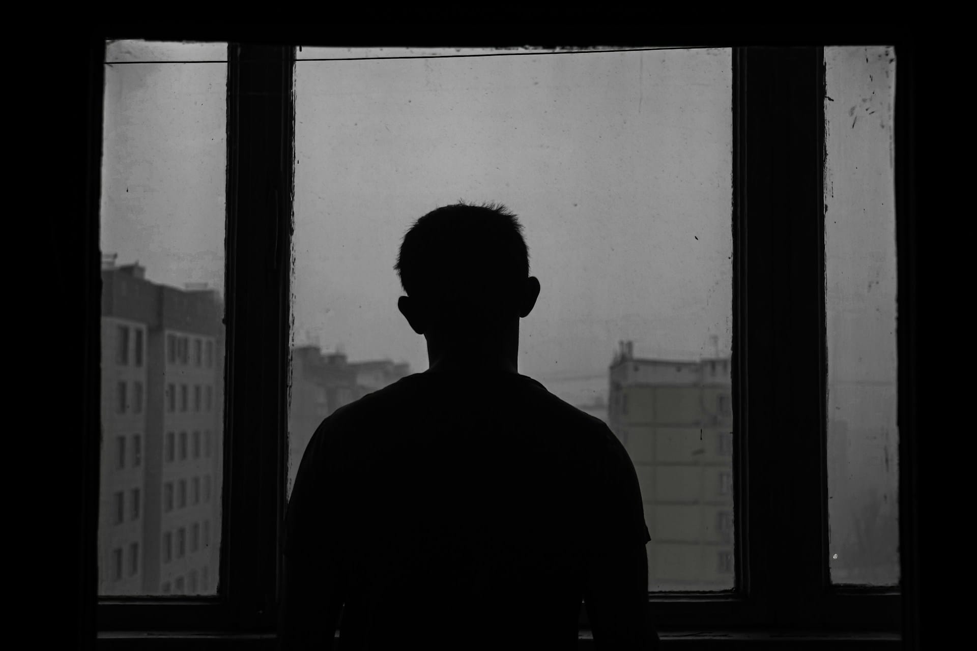Black and white silhouette of a person standing, facing a window.