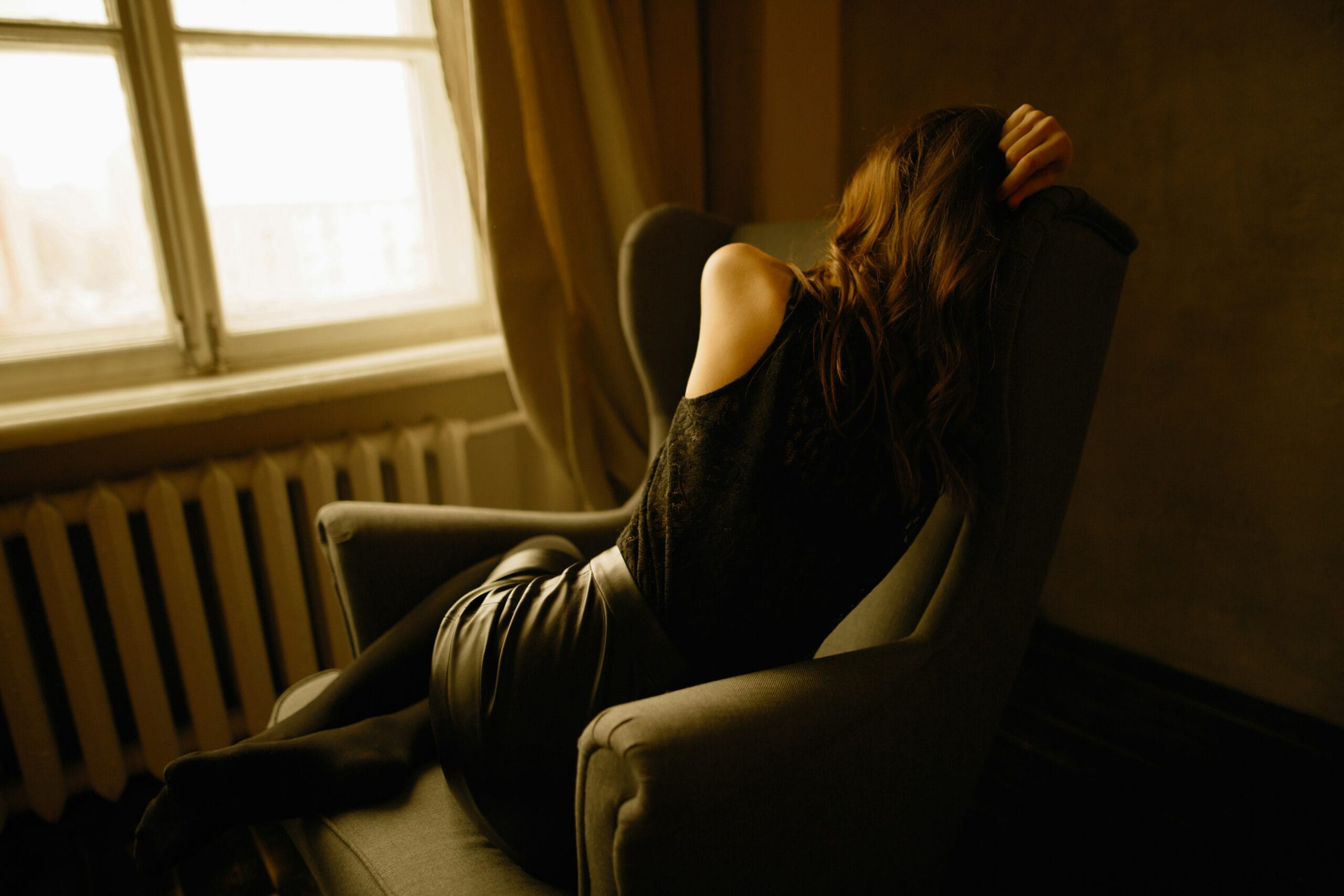 Woman curled up on chair next to a window.