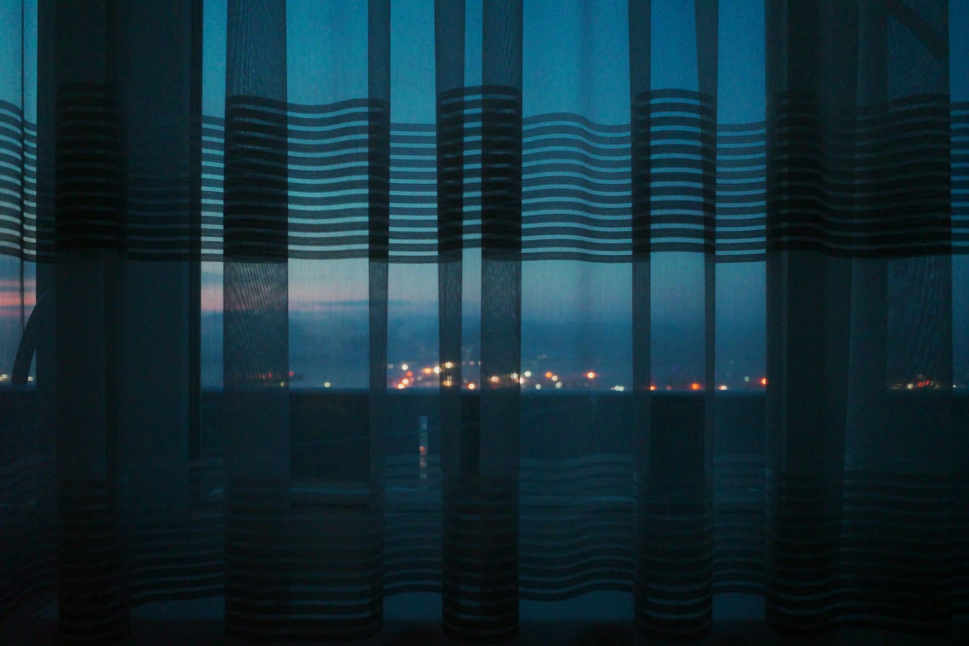 Facing the window in a dark room with the city lights in the background.