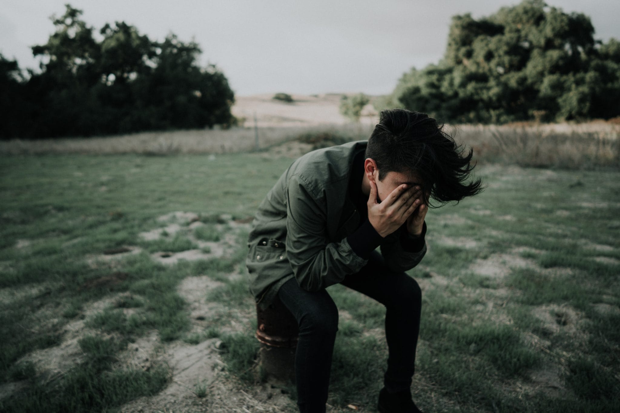 A person sitting with their head in their hands in a grassy field.
