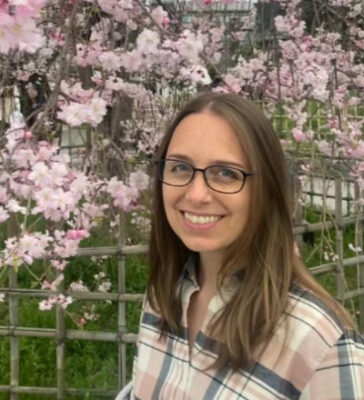 Heather Austin, smiling in front of a cherry tree in bloom.