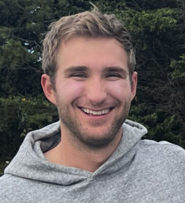 Jack Brandenburg, outside, smiling, wearing a grey hooded sweatshirt.