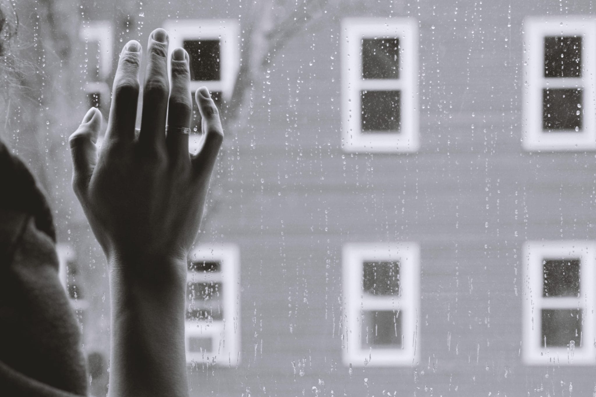 A person with their hand on the window on a rainy day.