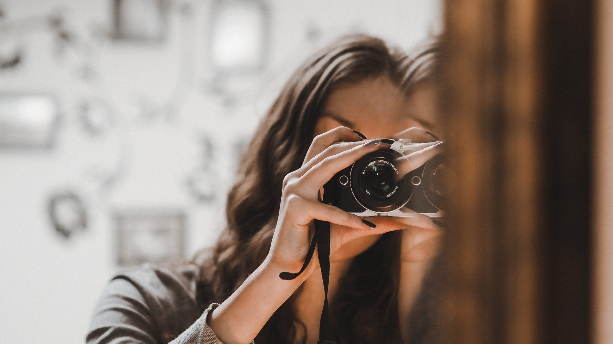 Woman taking a photo of herself with a camera in front of a mirror.