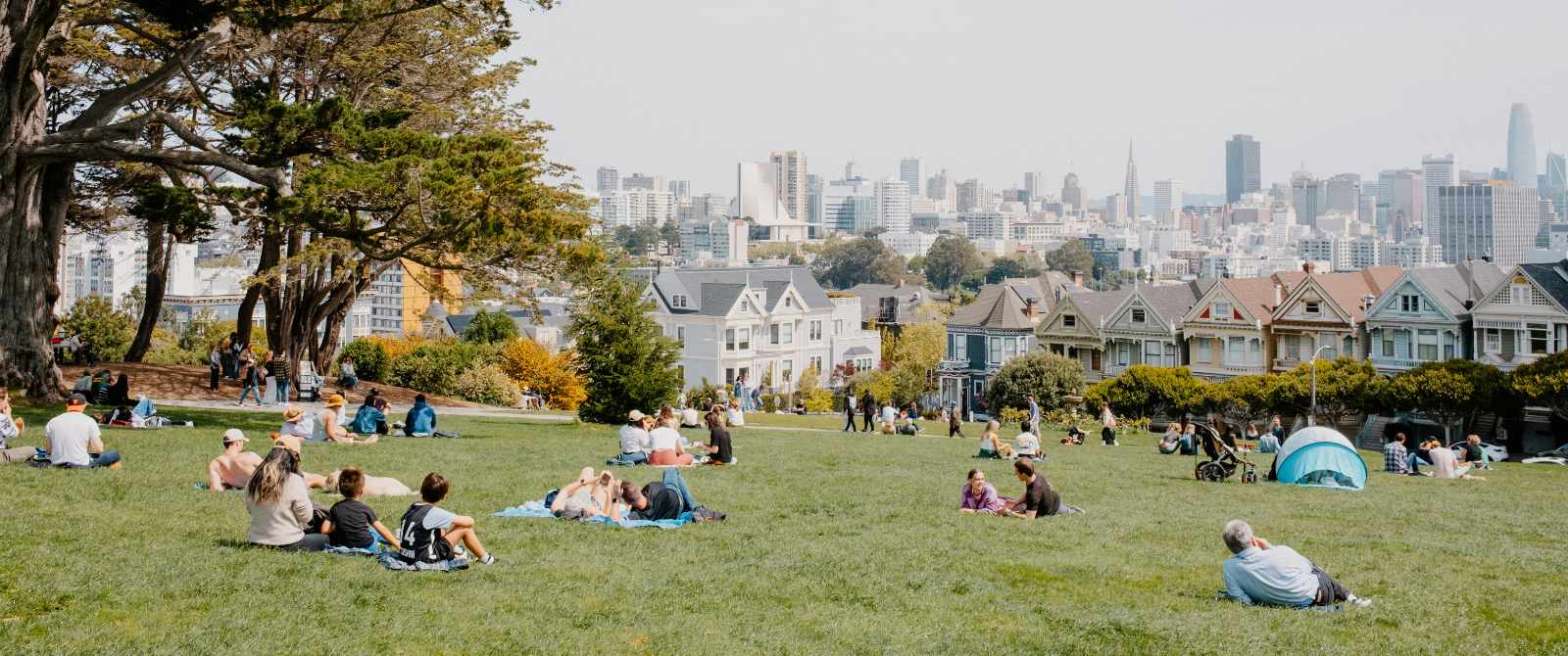 Families sitting on the grass at a park, overlooking downtown San Francisco in the background.