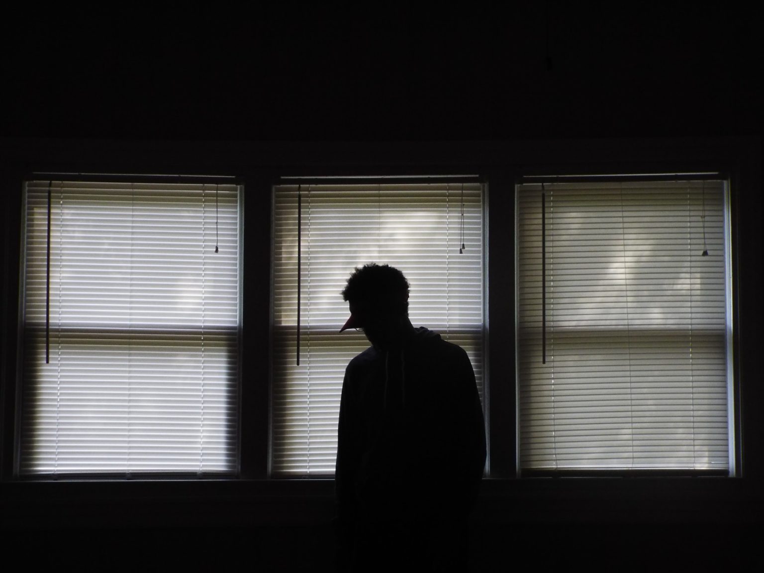 Person standing in front of windows with the blinds closed.