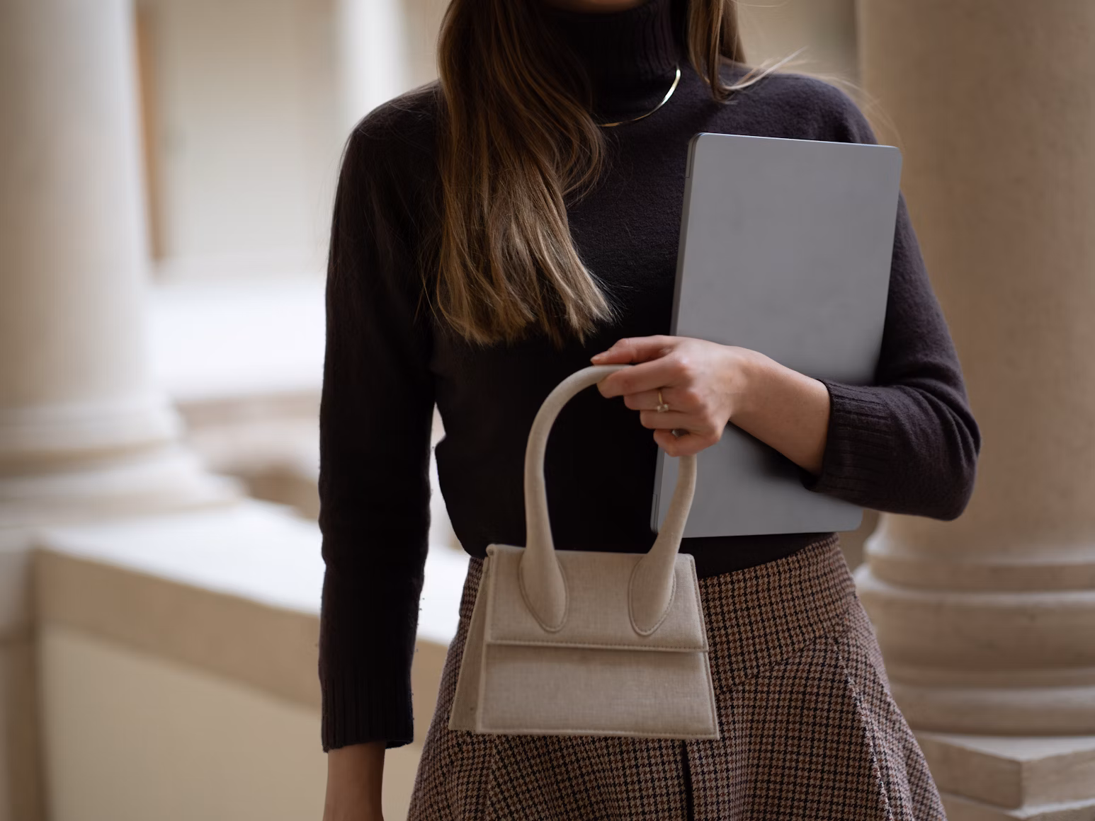 Woman in business casual attire, holding her purse and laptop.