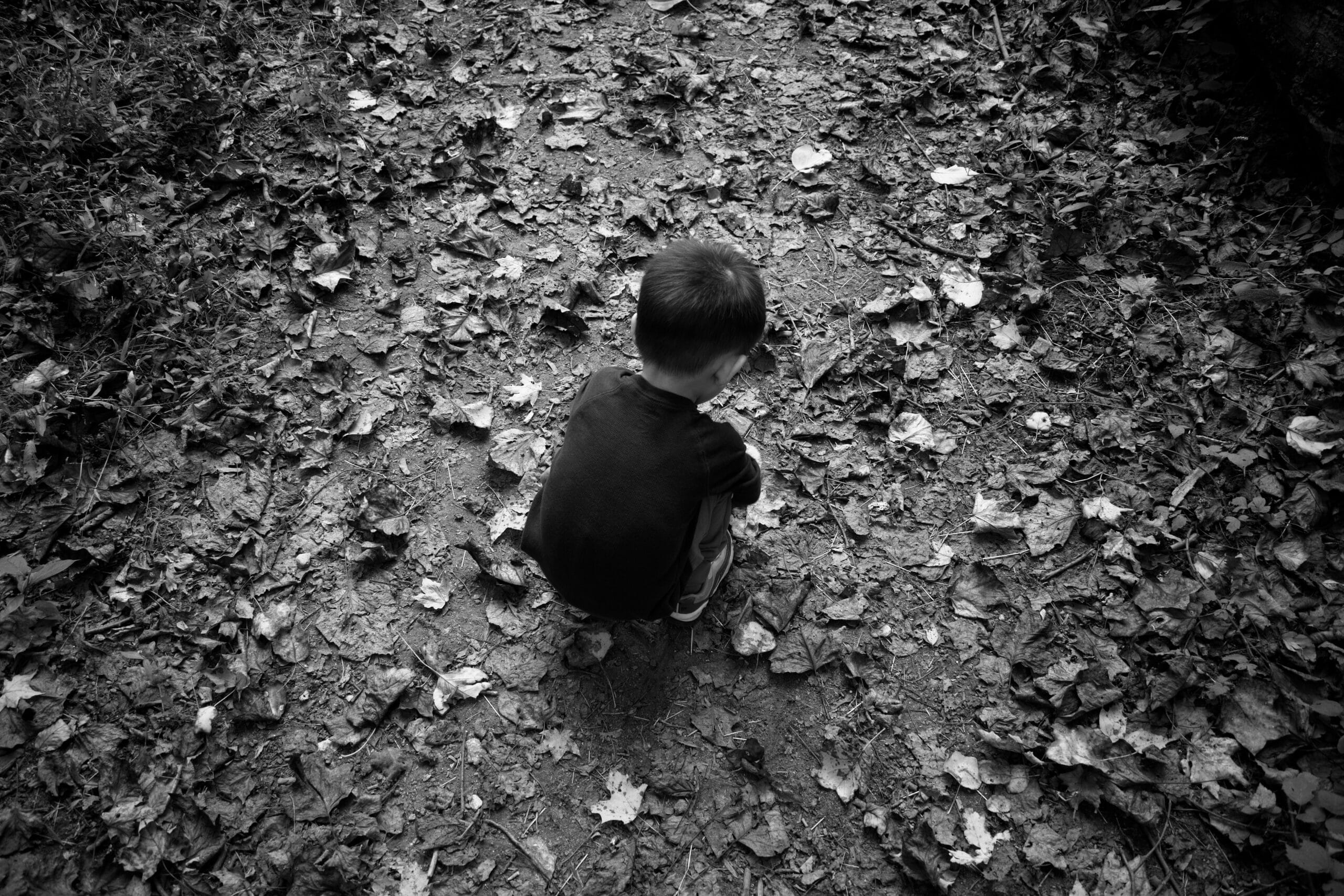 Black and white of child crouching down looking at the ground.