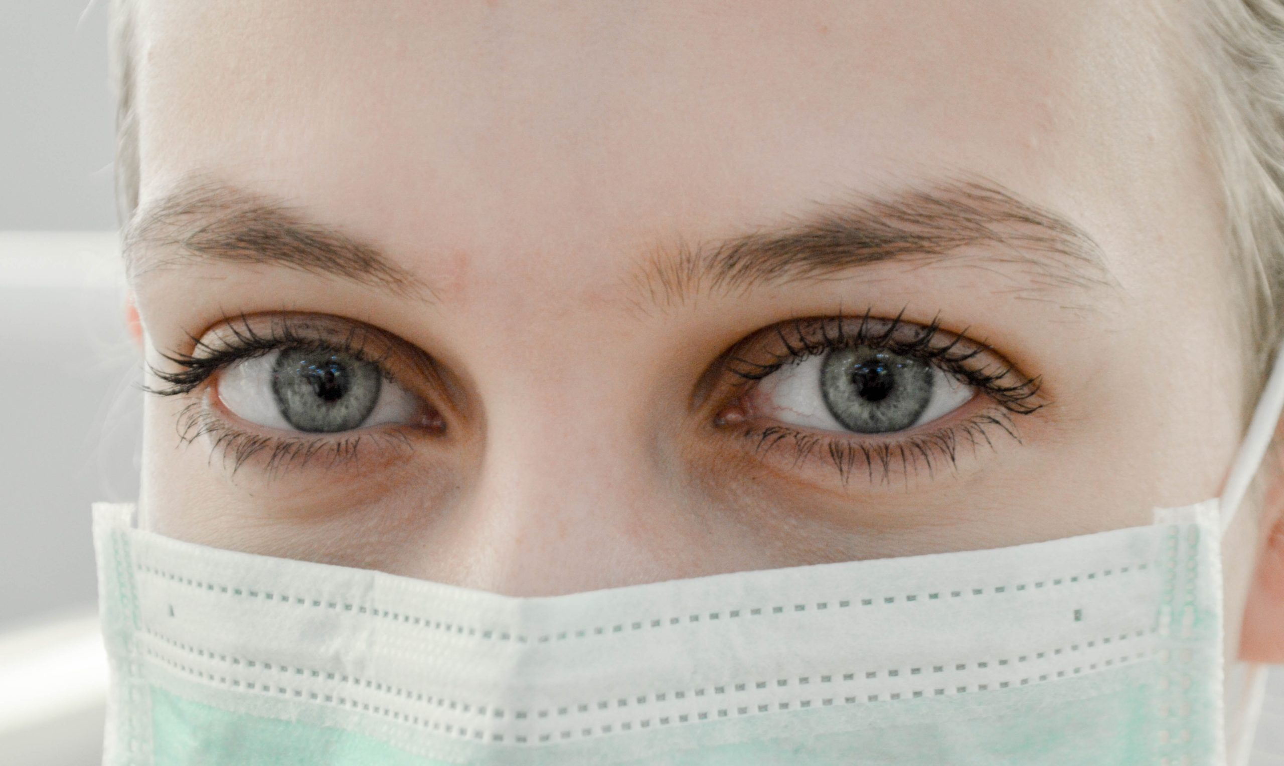 Close-up photo of a woman's eyes and the rest of her face covered by a surgical mask. 