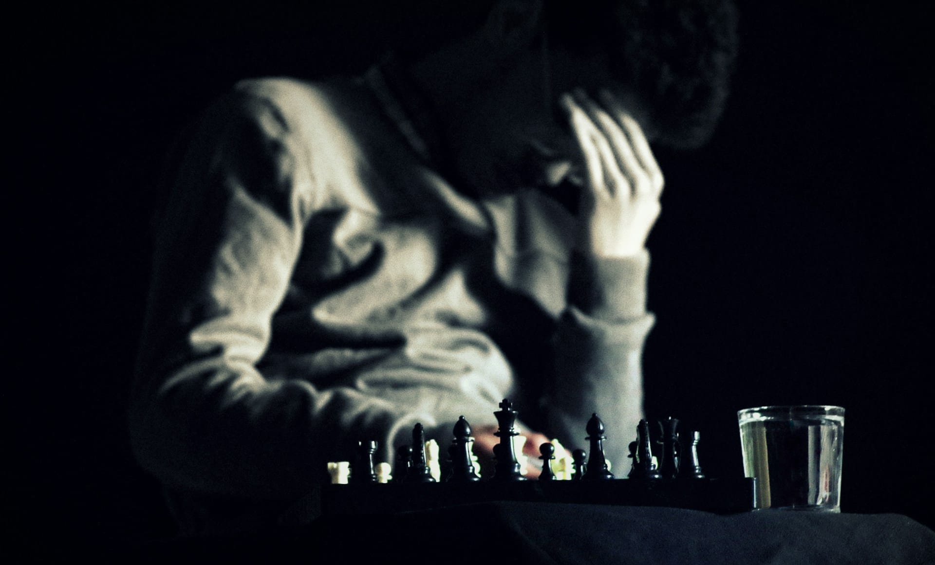 A man looking down with his fingers to his forehead, sitting at a table with a chess board.