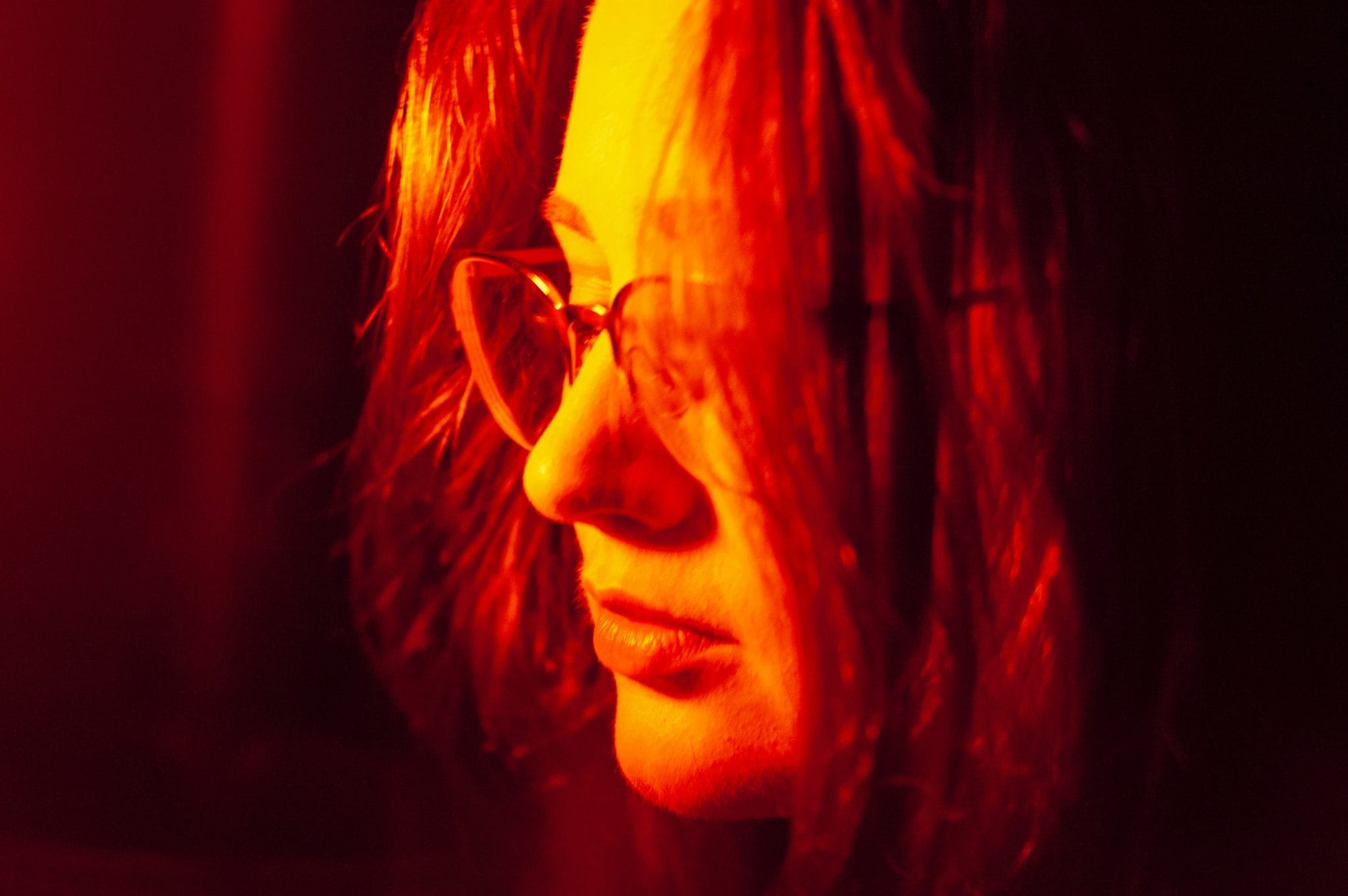 Close-up of a woman with a neutral expression in red light.