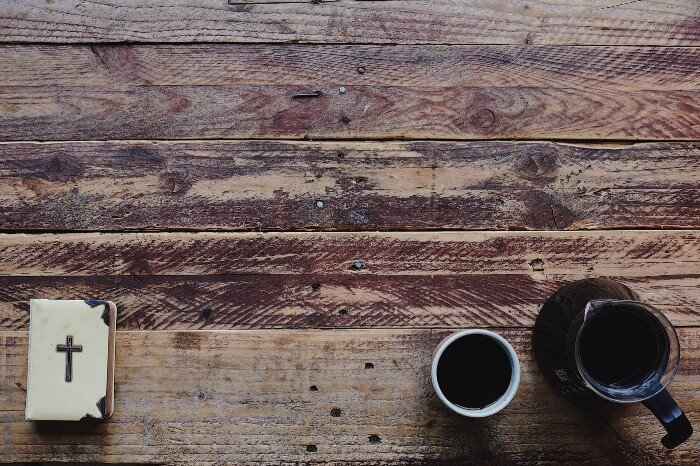 Wooden table with a small Bible and a cup of coffee.