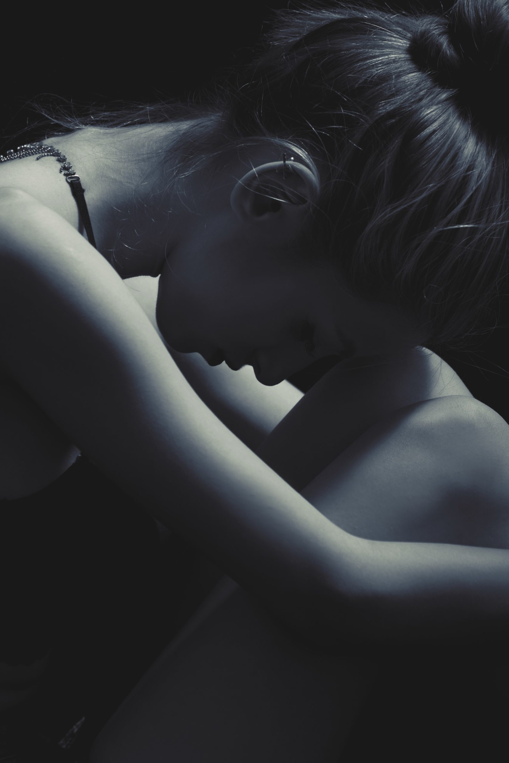 A woman with her head down and arms wrapped around their legs in a dark setting.